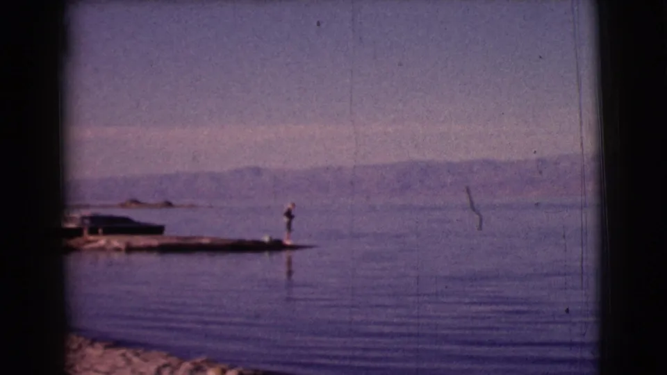 Final 1961 8mm frame from Clarkdale, Arizona, showing a small lakeside pier, distant person, calm water, and low hills.