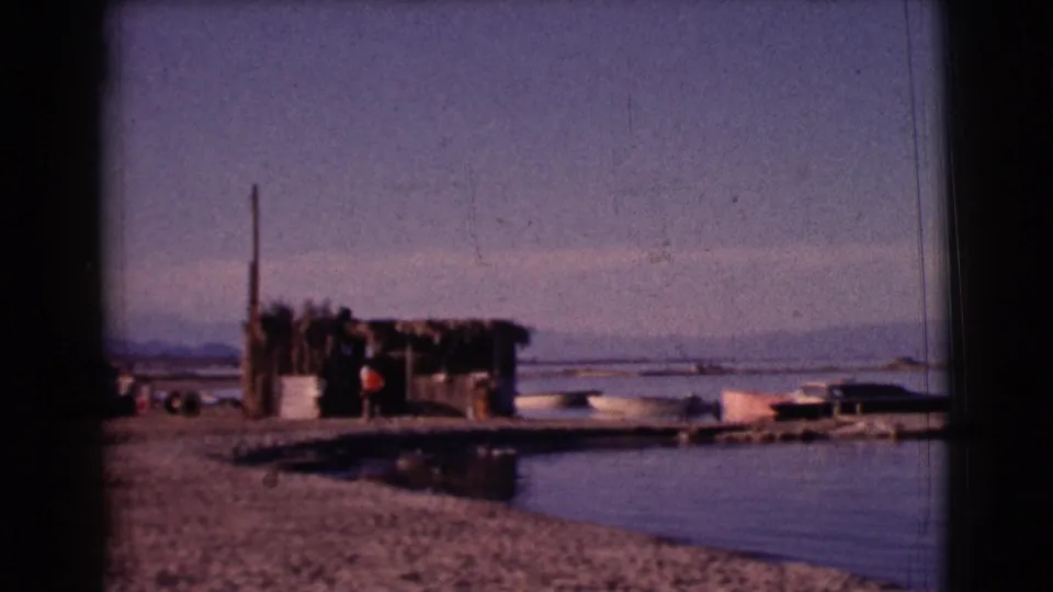 1961 Clarkdale, Arizona home-movie view of a rustic lakeside shelter, small boats, water, and a gravel shore.