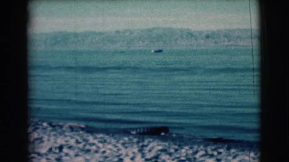 1961 Clarkdale, Arizona 8mm view of a quiet lake, low shoreline waves, rocky foreground, distant hills, and a tiny boat offshore.