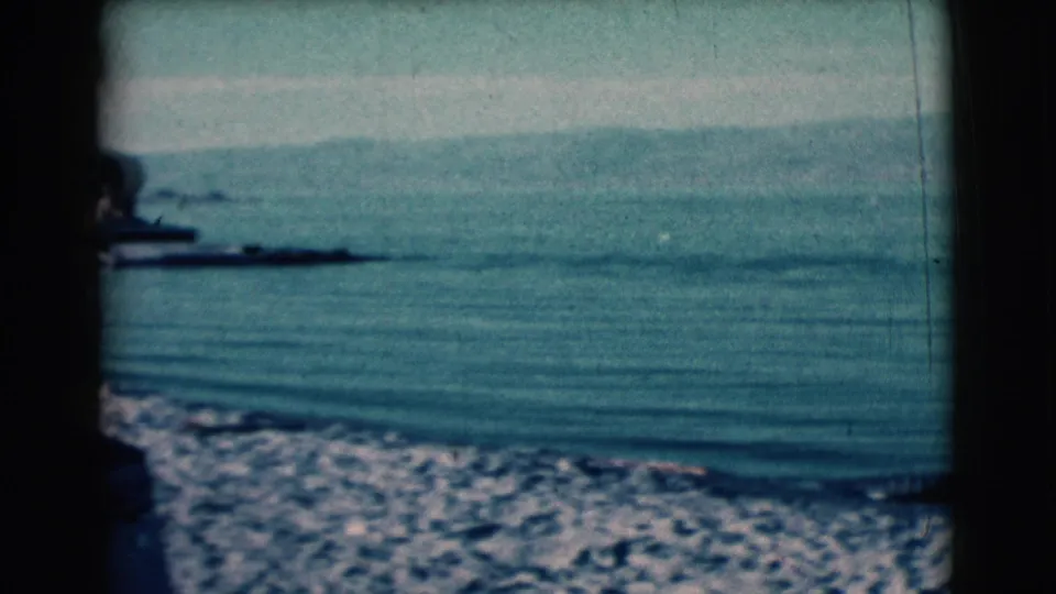 1961 Clarkdale, Arizona frame showing a tranquil lake, rocky shoreline wash, faint hills, distant boats, and dark 8mm frame edges.