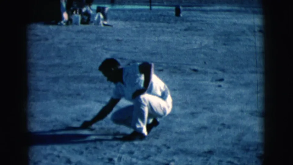 In Clarkdale, Arizona, 1961, a man in light clothing crouches on dusty ground and reaches toward marks in the dirt.