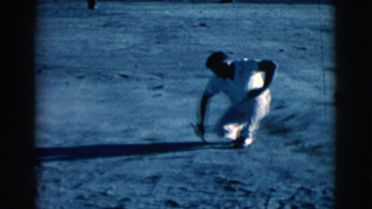 Man in white clothing crouching on dusty ground with one hand near the dirt.