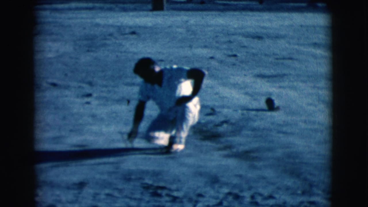 Man crouched on open dirt, leaning forward with one arm extended.