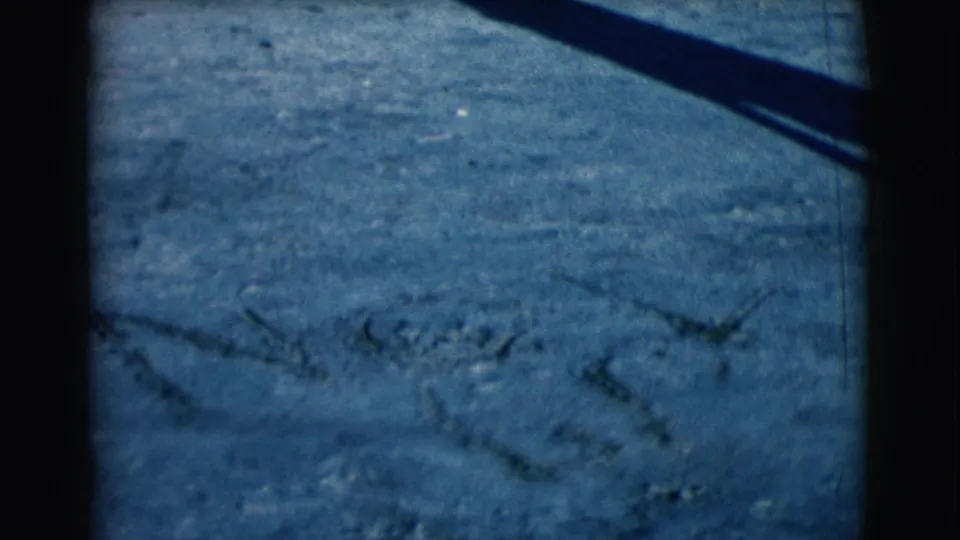 Blue-tinted 8mm frame of sandy ground in Clarkdale, Arizona, with rough markings and a dark diagonal shadow.