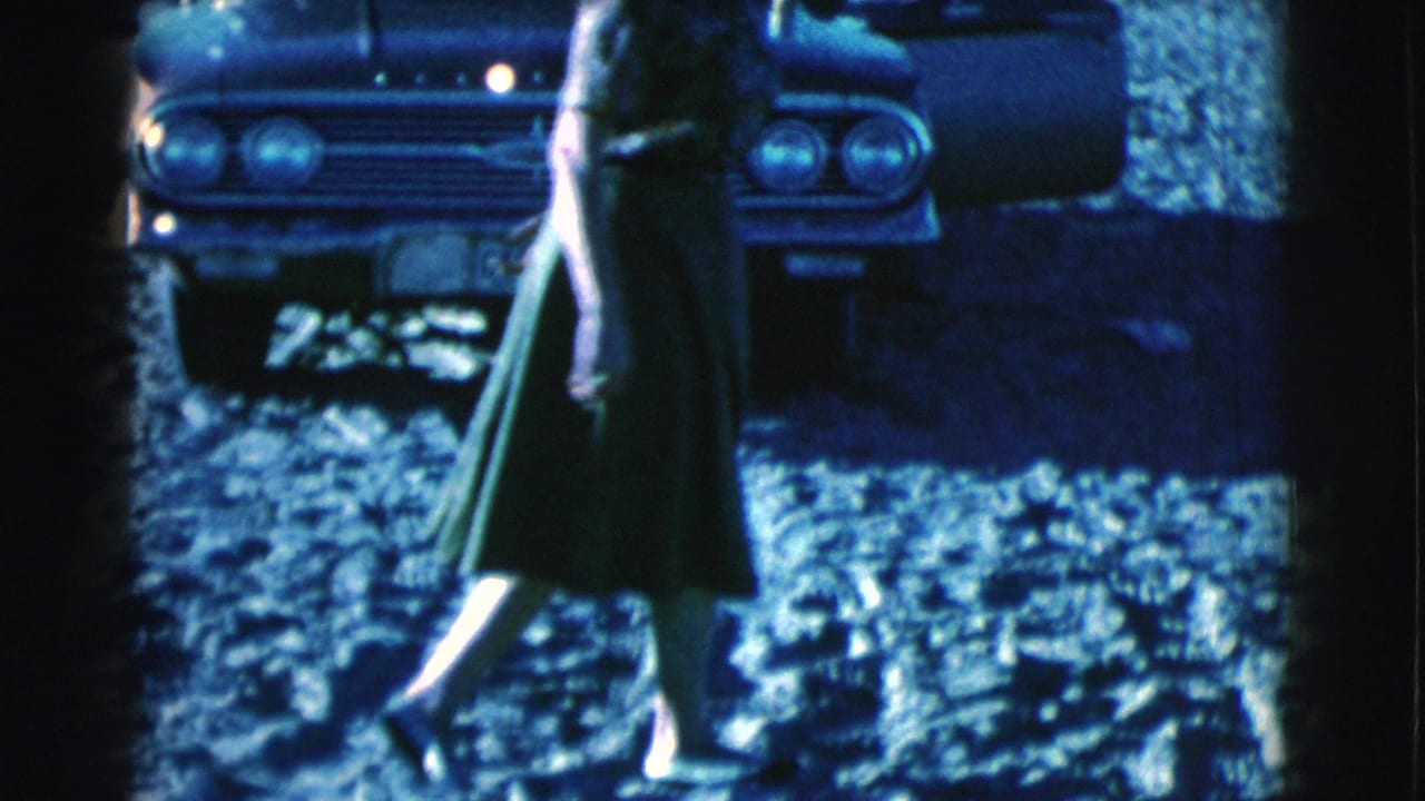 Woman walking across sandy ground in front of a parked car.