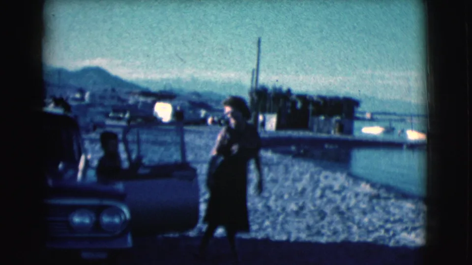 The woman appears to hold a hand or object near her face while walking by the vintage car along the water in Clarkdale, Arizona.