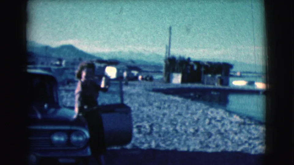 The handheld 8mm view shows the woman beside the car door, with Clarkdale shoreline, water, and low mountains in the background.