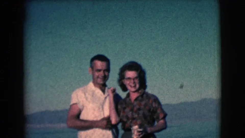 In 1961 Clarkdale, Arizona footage, a man in a white short-sleeved shirt stands beside a woman with glasses near water and hills.