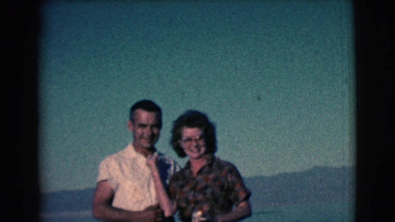 Smiling couple stands close together outdoors, with the woman holding a cup.