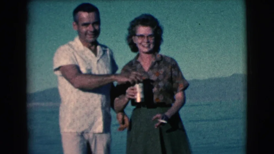 In 1961 Clarkdale, Arizona home-movie footage, a smiling couple stands near water, holding drinks with distant hills behind them.