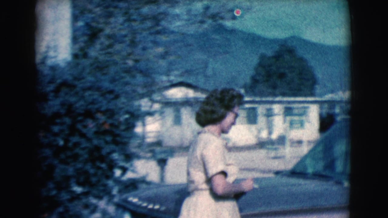 In 1961 Clarkdale, Arizona home-movie footage, a woman approaches a classic station wagon in a suburban neighborhood with trees and mountains beyond.