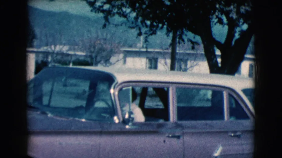 1961 Clarkdale, Arizona home-movie frame showing a light station wagon with dark roof beside trees and modest houses.