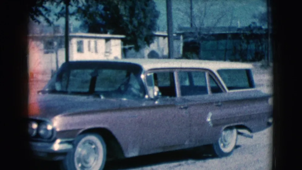 A 1961 Clarkdale frame shows the station wagon from the front side, with whitewall tires, tree shade, and homes behind it.