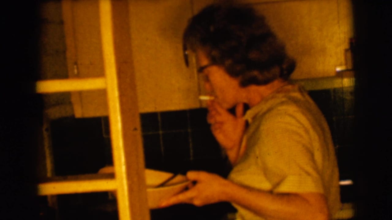 Woman in glasses smokes in a dim kitchen while holding a bowl near a ladder.