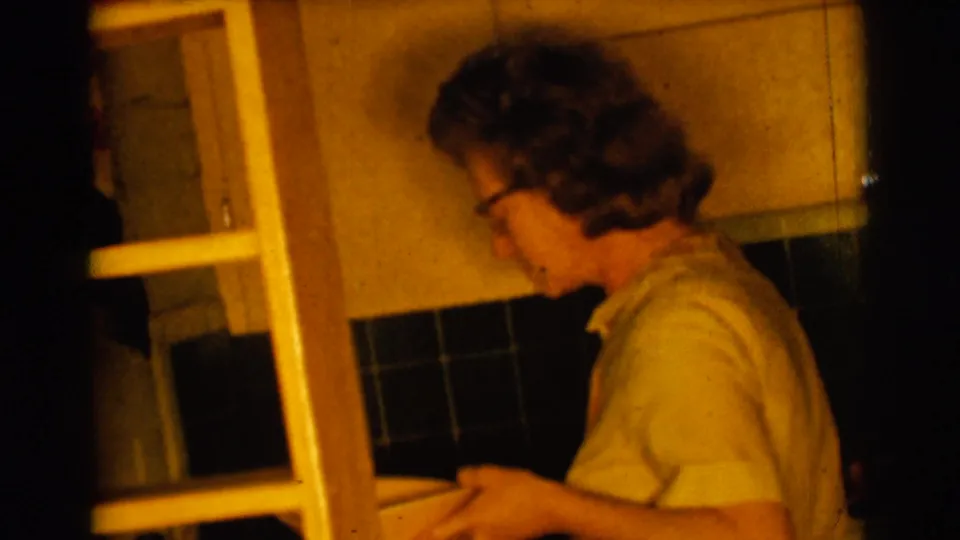 The woman stands in profile inside the Clarkdale kitchen, holding a bowl beside cabinets and a dark tiled backsplash.