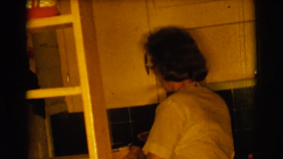 The woman turns partly away from the camera in the same 1961 home kitchen, with a ladder and dark backsplash visible nearby.