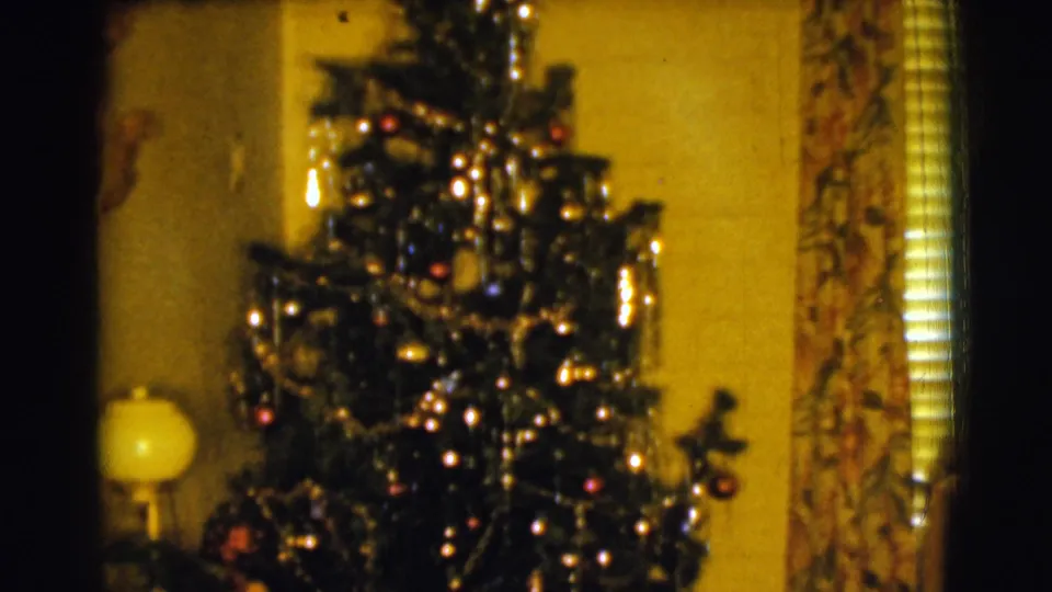 1961 home-movie frame from Clarkdale showing the tree lower in the room, with a lamp, ornaments, tinsel, curtain, and blinds visible.