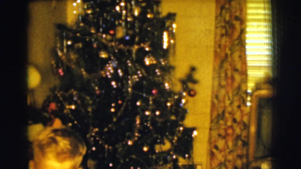 Final 1961 Clarkdale frame showing the decorated Christmas tree in a private room, with curtains, blinds, and a partial person near the foreground.