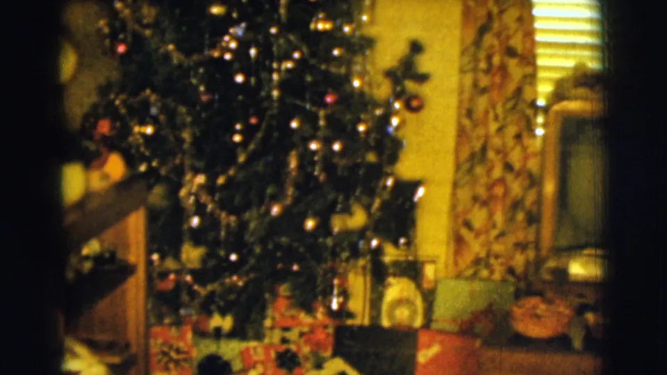 1961 Clarkdale home-movie frame with a lit Christmas tree, wrapped presents, curtains, and household objects in a private living room.