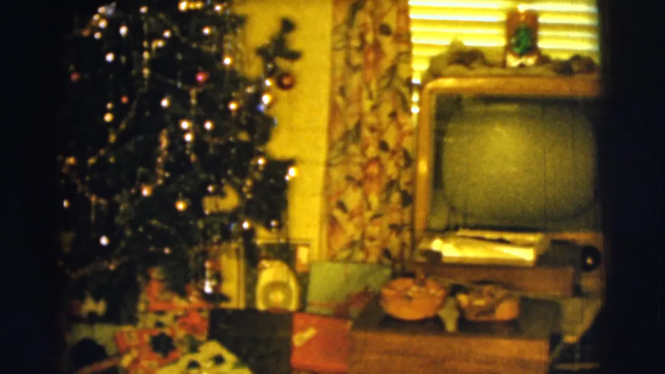 1961 Clarkdale home-movie frame with Christmas tree lights, presents, a console television, curtains, and small household decor.