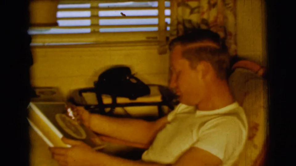 The young man smiles toward the record album in a 1961 Clarkdale home interior with blinds, curtains, and a black rotary telephone behind him.
