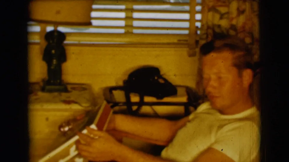 In a 1961 Clarkdale, Arizona home interior, a man in a white shirt sits with a book near a lamp, side table, and black telephone.