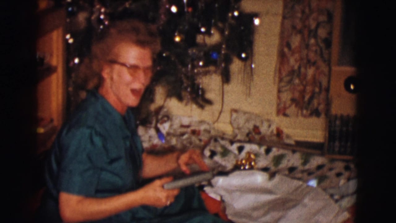 Woman in glasses seated by a Christmas tree holding a wrapped gift.