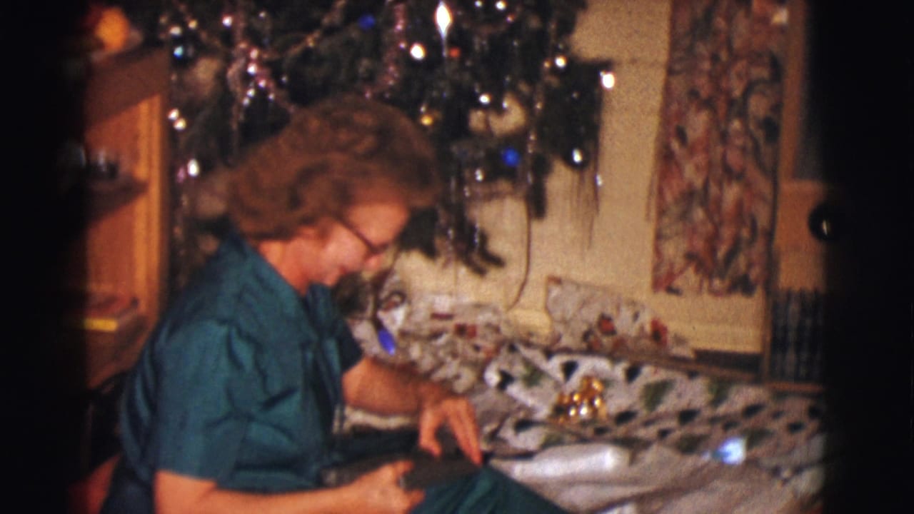 Woman seated beside the tree looking down at a present in her lap.