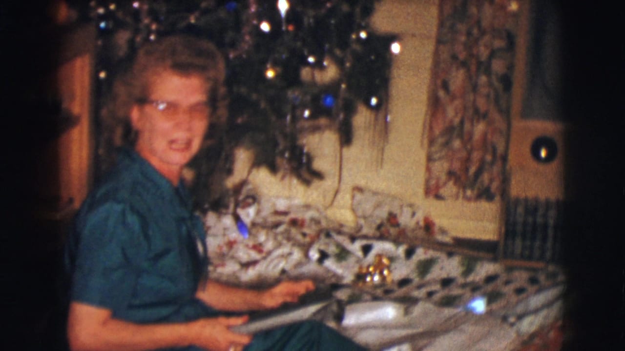 Woman in glasses sits near a decorated Christmas tree with wrapping paper on a couch.