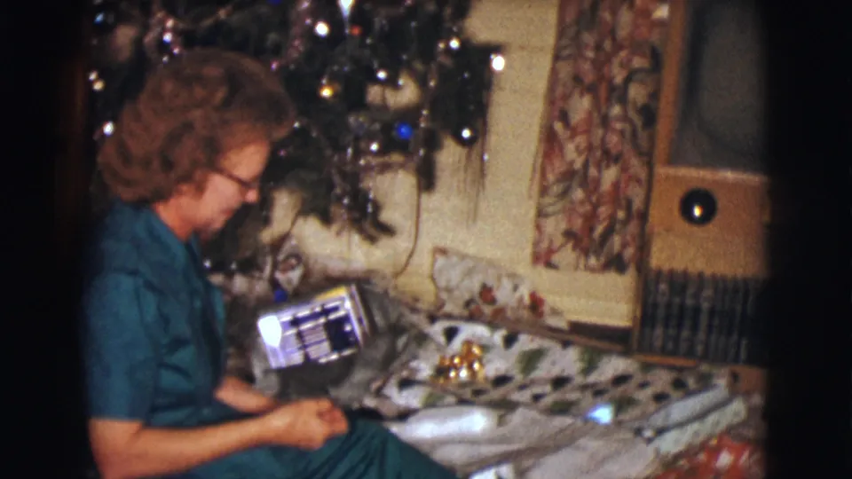 The woman holds up a reflective rectangular gift package while seated beside the decorated tree in Clarkdale, Arizona.