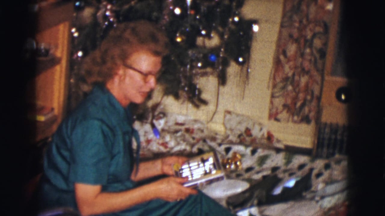 Woman seated by the Christmas tree holds a rectangular wrapped gift.