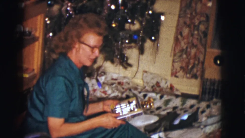 The woman sits beside the Christmas tree in the 1961 Clarkdale home interior while handling a rectangular present.