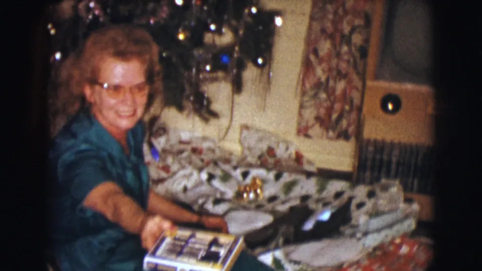 The smiling woman reaches forward with a present in the Clarkdale Christmas home-movie scene from 1961.