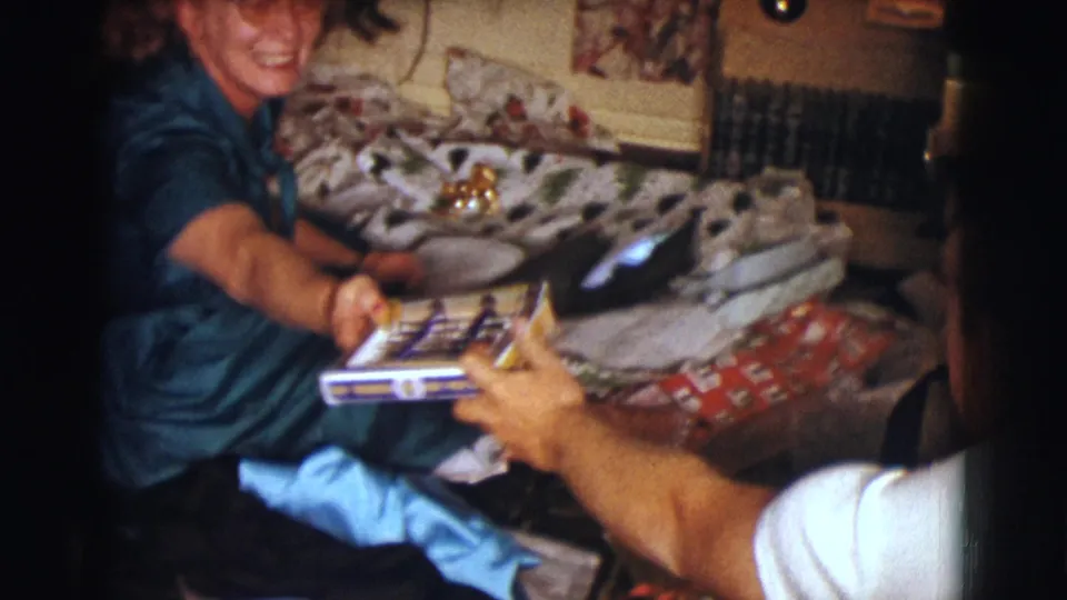 A woman in the 1961 Clarkdale Christmas scene hands a present toward an off-camera person whose arm is visible.