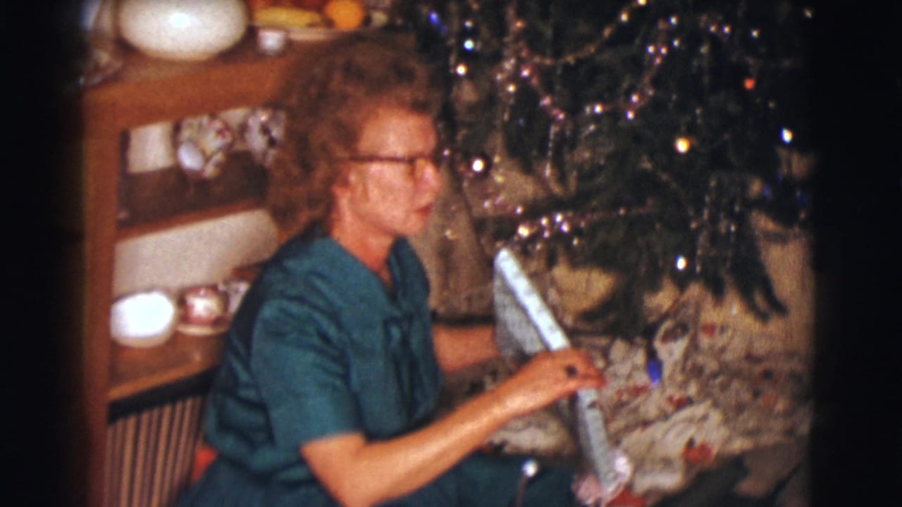 Woman beside the Christmas tree begins opening a long wrapped package.