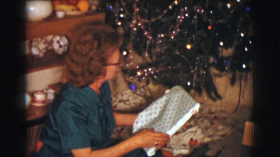 The woman holds the opened wrapping paper and looks toward the decorated Christmas tree inside the private Clarkdale holiday room.