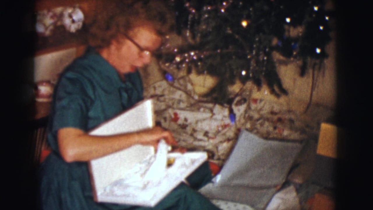 Woman in a green dress opens a box beside a decorated Christmas tree.