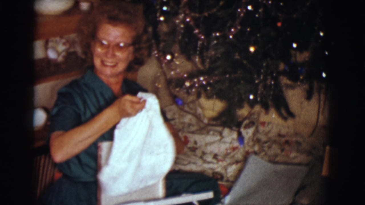 Woman smiles toward the camera while lifting white fabric from a gift box.