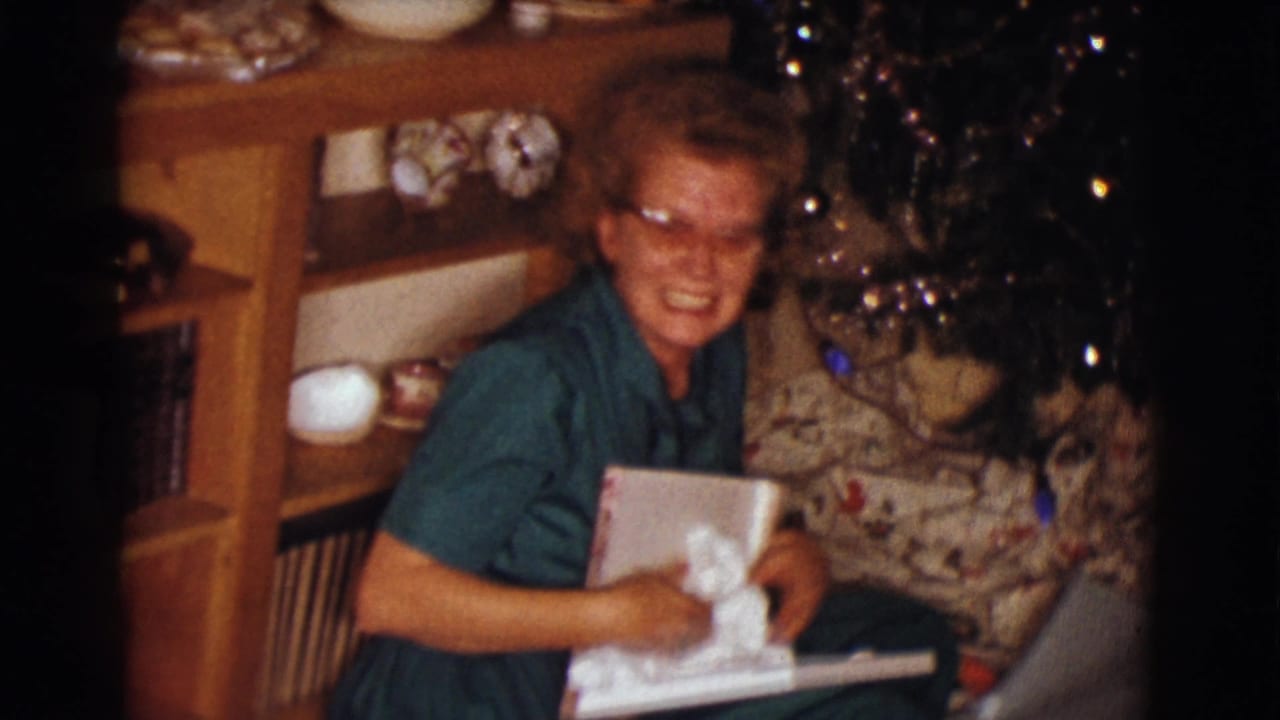 The woman laughs during the gift opening, holding a white garment or package in a decorated Clarkdale living room.