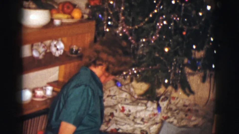 The woman turns away toward the decorated tree in the private living room at the end of the gift-opening moment.