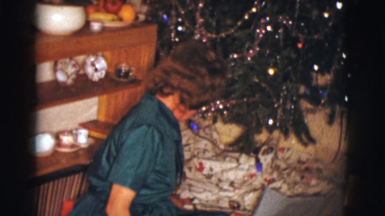 Woman in a green dress sits beside wrapped gifts under a decorated Christmas tree.