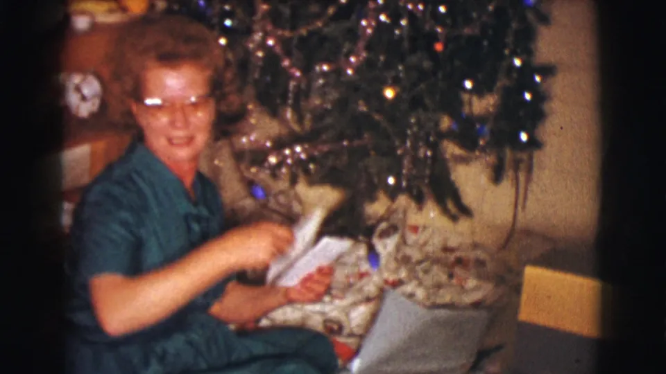 The woman sits by the Christmas tree in a private Clarkdale interior, holding white envelopes among wrapped gifts.
