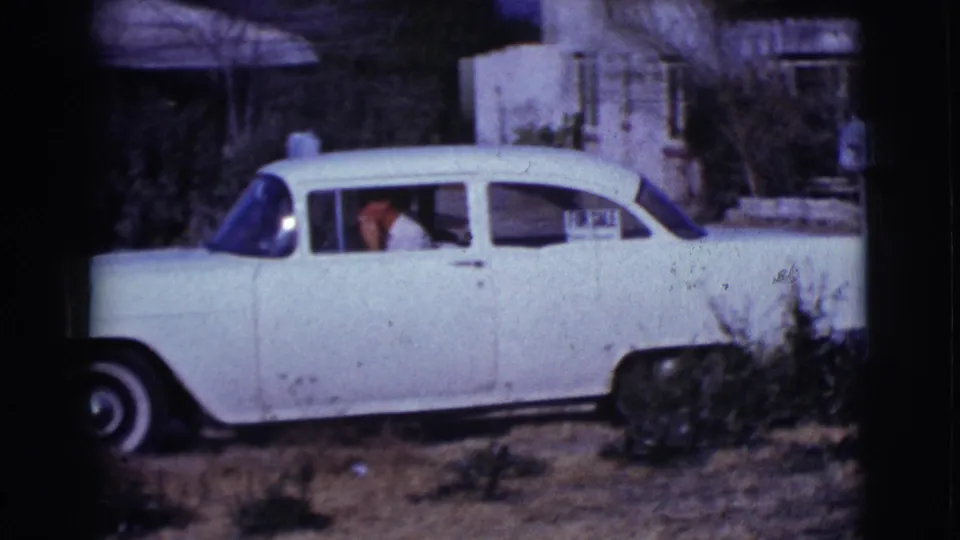 A white early-1960s sedan fills the frame, with a man visible inside or beside the front seat in Clarkdale, Arizona footage.