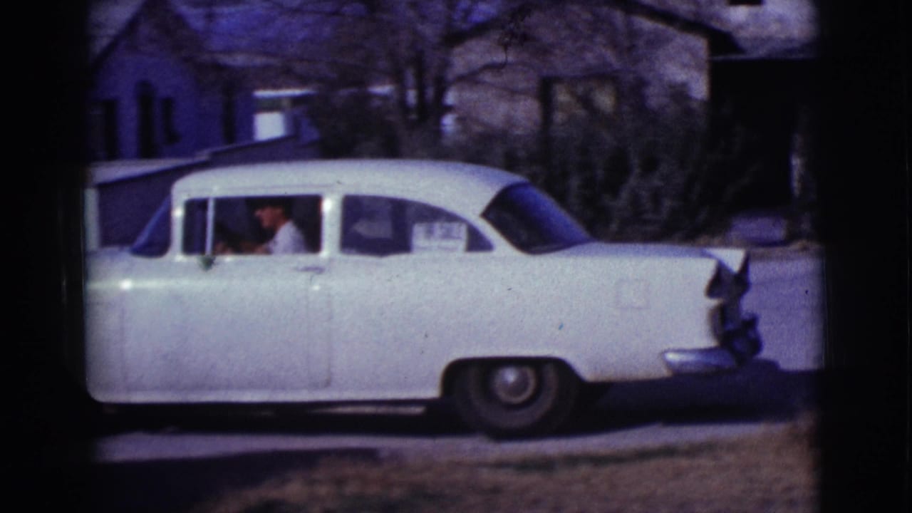 White sedan parked beside a house with a person visible through the side window.