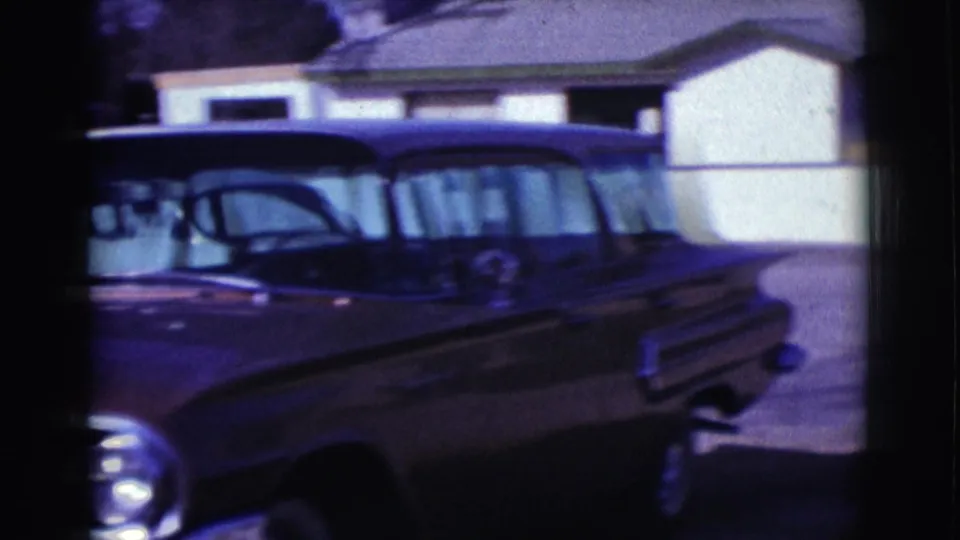 Dark mid-century station wagon seen from the side in the 1961 Clarkdale residential street footage.