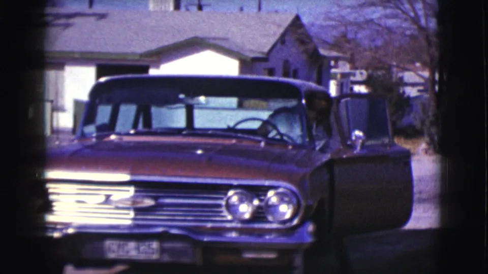 Red Chevrolet-style car faces the camera with an open door, chrome grille, and residential houses behind it in 1961 Clarkdale footage.