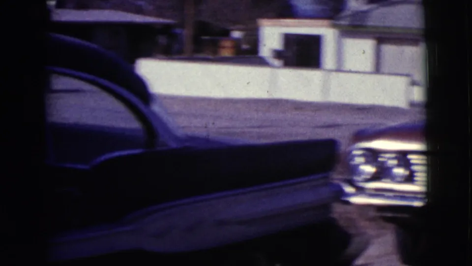 1961 Clarkdale, Arizona frame where the camera pans past a dark car side while the red sedan remains partly visible.