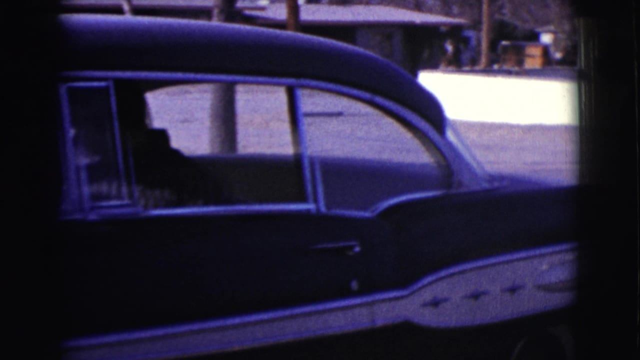 Dark sedan parked in a driveway with a man visible through the side window.