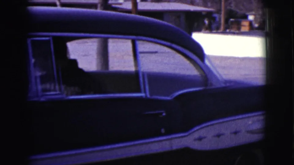 1961 Clarkdale, Arizona home-movie frame showing a dark mid-century sedan in a driveway with a man seated inside.