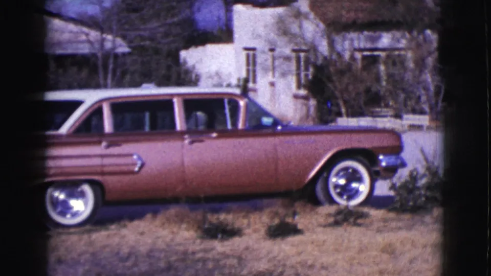 1961 Clarkdale frame showing a reddish-brown station wagon beside dry grass, with a residential home in the background.